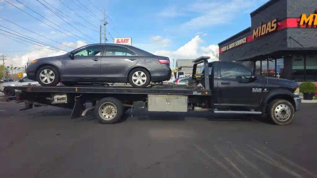 Hook Em' Up Towing flatbed loaded with a Toyota Camry outside a Nashville Midas auto shop