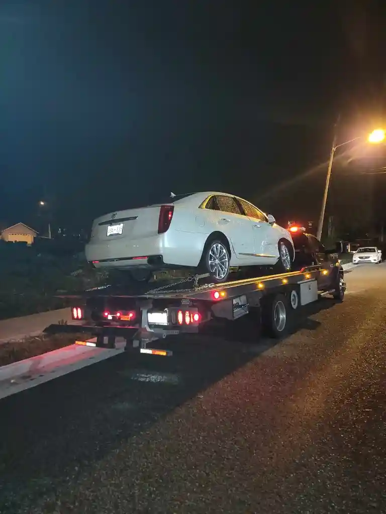White Cadillac sedan secured on a Hook Em' Up Towing flatbed at night in Tennessee