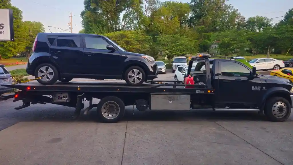 Hook Em' Up Towing flatbed transporting a black Kia Soul SUV through a Nashville neighborhood