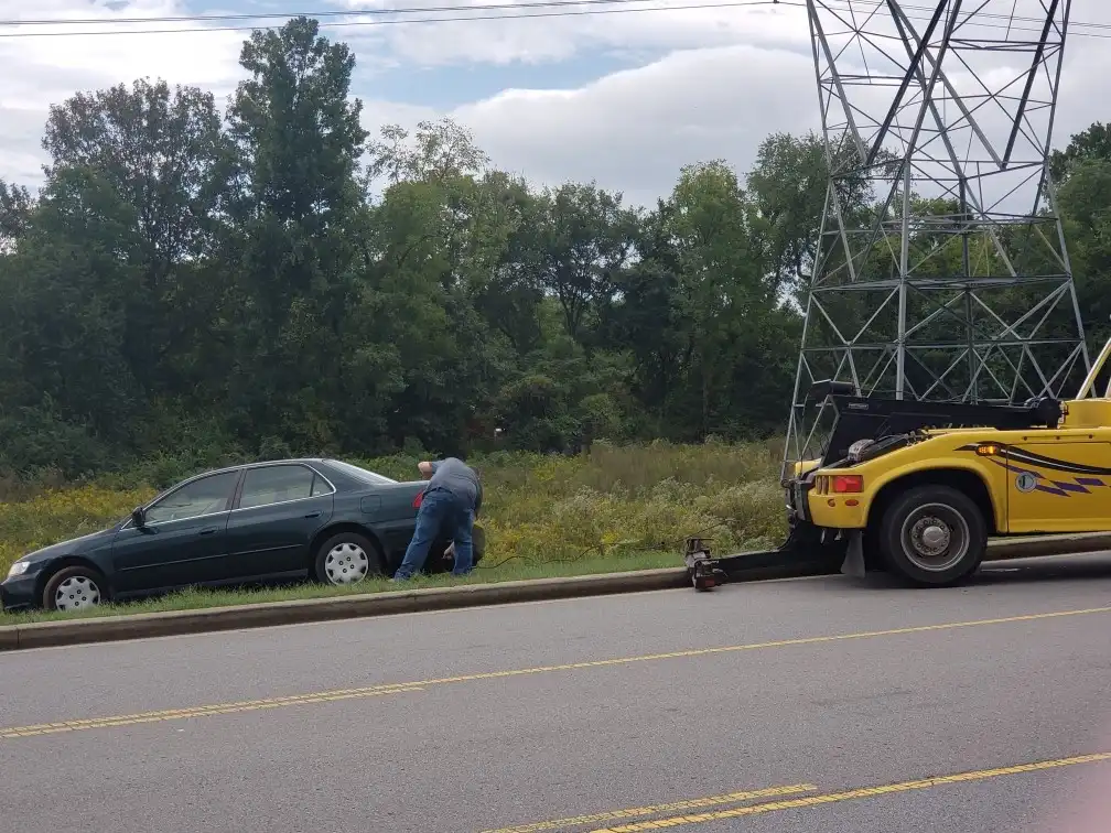 Tow truck operator performing winch out recovery on sedan stuck in ditch in Nashville TN